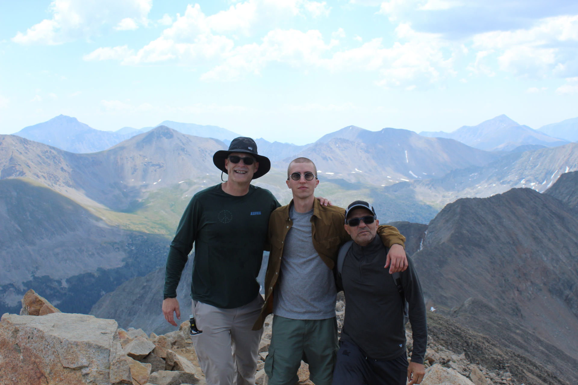 Three hikers with arms around each other on the summit of Huron Peak with the Sawatch Range behind